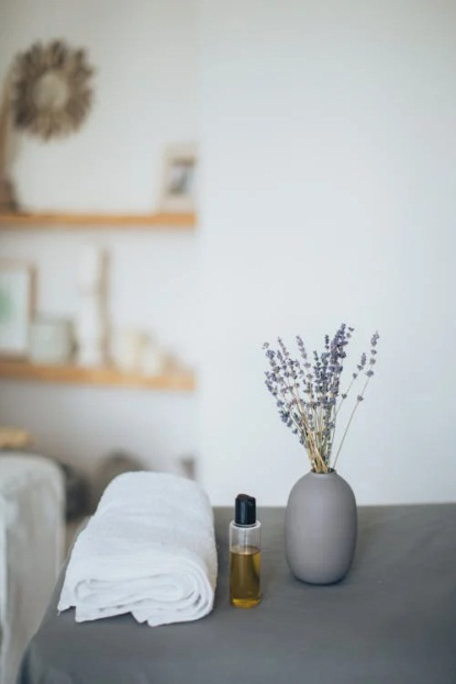 An image of an oil bottle, lavender plant, and towel on a table