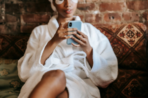 An image of a woman in a bathrobe sitting on a couch and using her phone