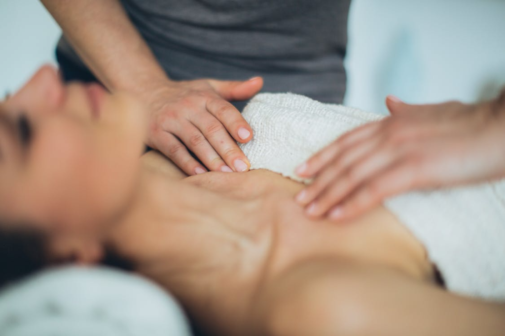 a woman lying down on a massage table with a masseuse massaging her chest