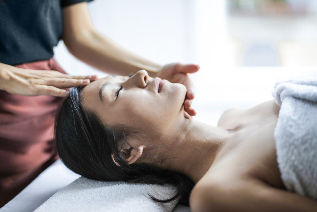 a woman lying down on a table with a towel over her, getting a head massage therapy