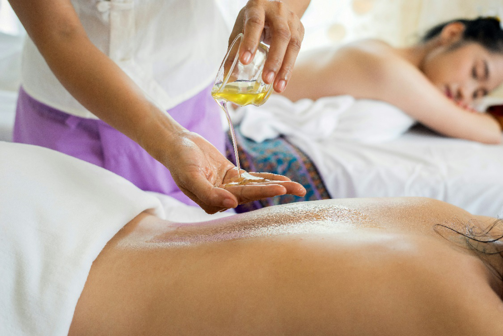 Therapist pouring massage oil onto a client’s back during a couples massage session in a spa.