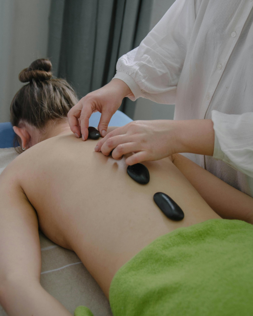 Woman receiving hot stone massage therapy on back with therapist placing heated stones