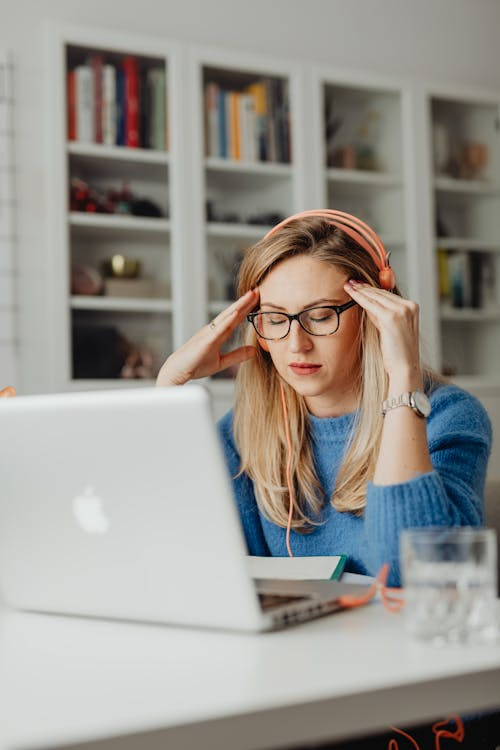 An image of a woman holding her head while working on her laptop
