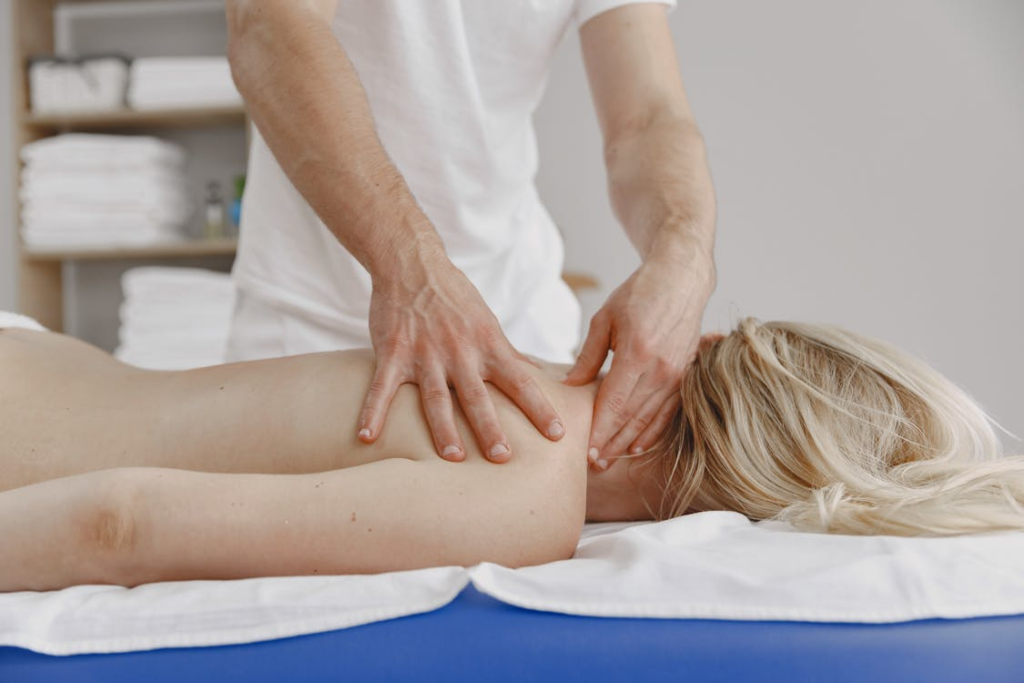 a blonde woman lying upside down on a white wheel getting a deep tissue massage by a masseuse 