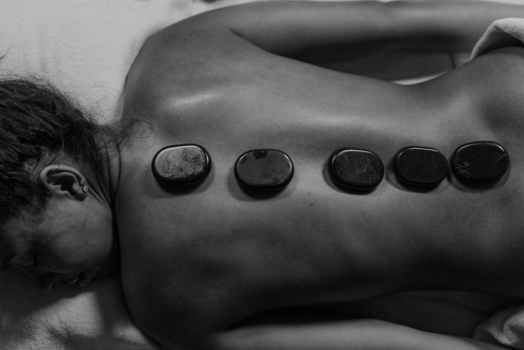 This photo shows a woman lying flat with massage stones on her back.