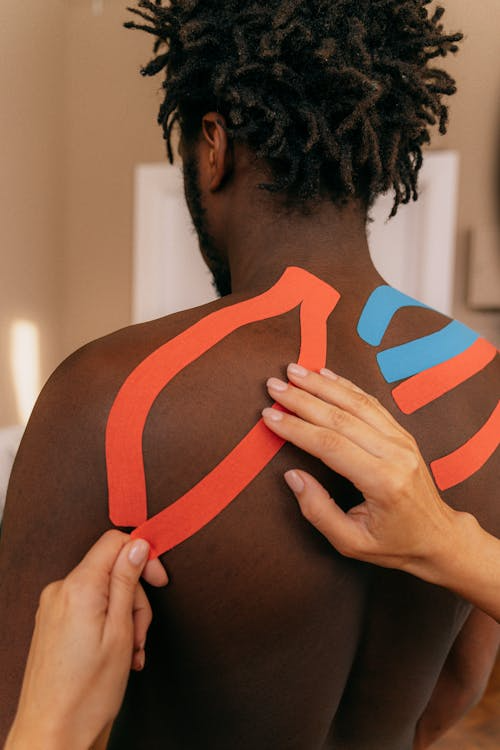 a therapist applying kinesiology tape to a person’s shoulder and upper back